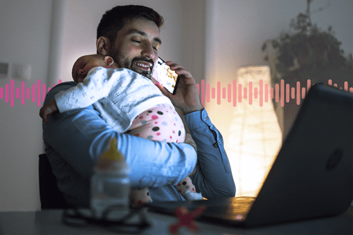 A smiling father holding a sleeping child while using a mobile phone